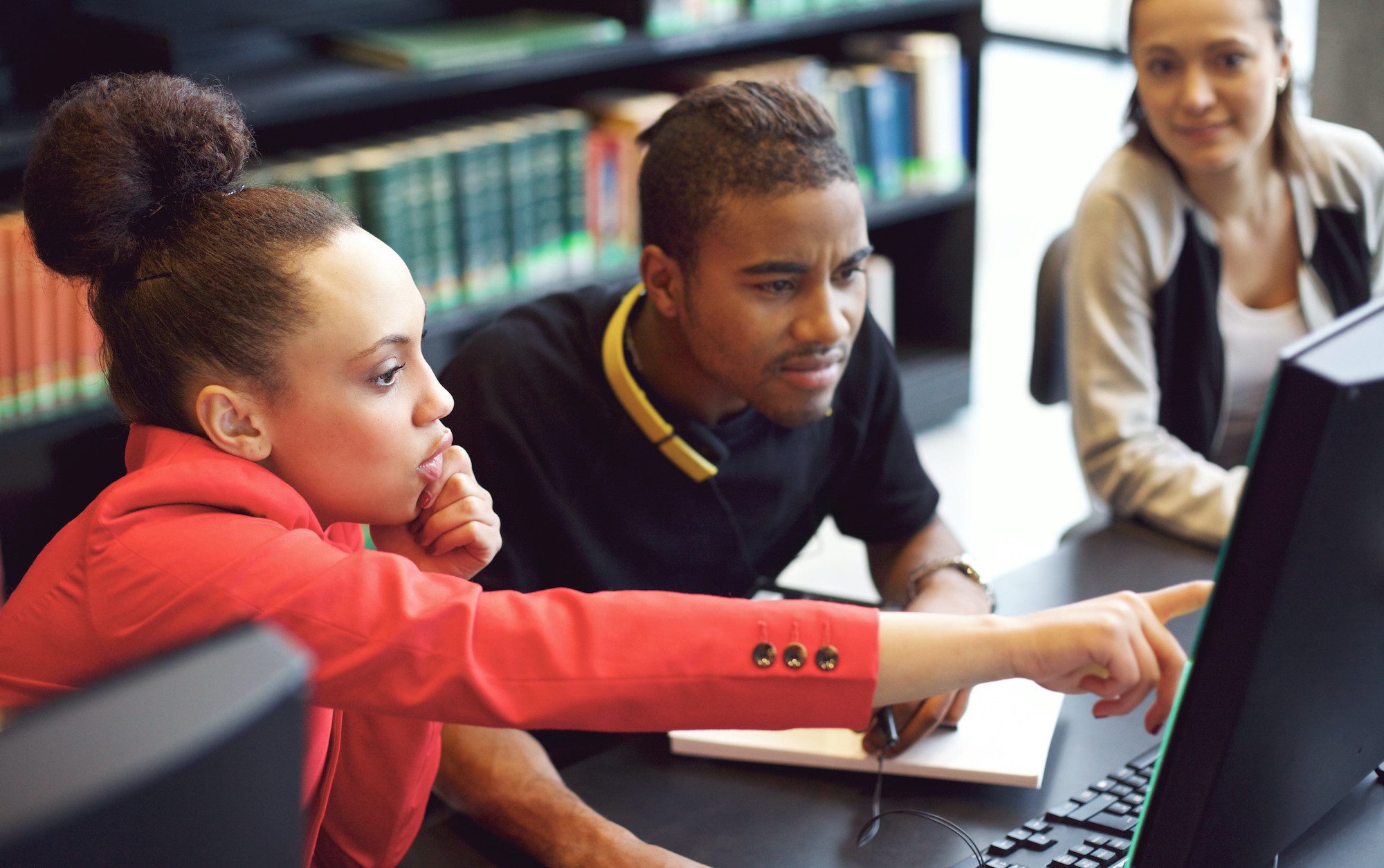 Girl red jacket teaching young man with headphones about computer programs